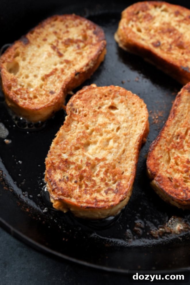 Close-up of two slices of sourdough French toast frying in a cast iron skillet, showing the golden-brown crust forming and butter sizzling around them.