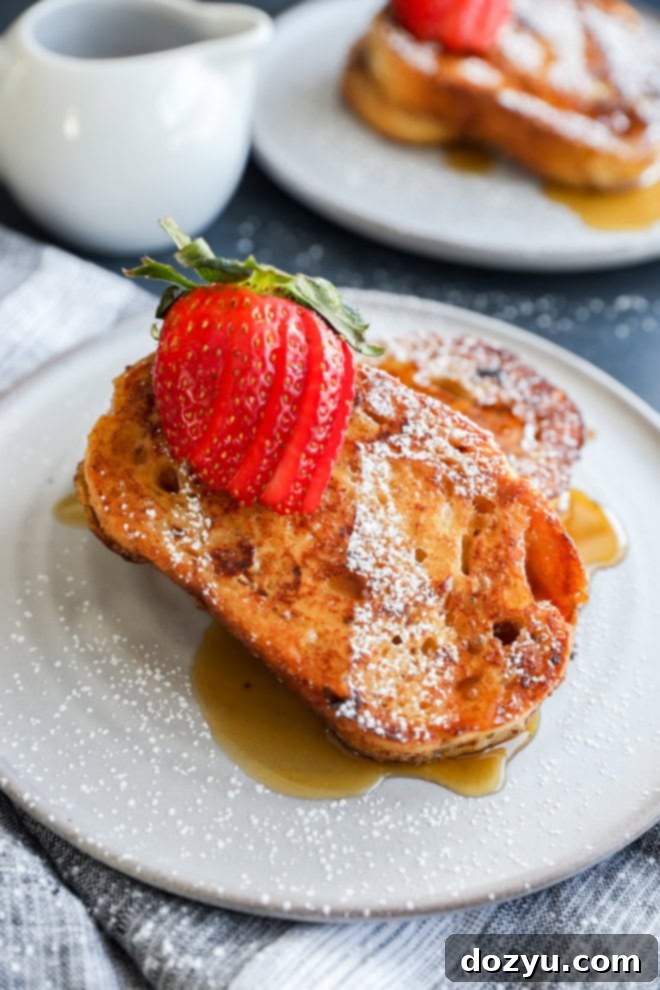A close-up shot of a single slice of sourdough French toast on a plate, ready to be eaten, with a fork gently piercing it, showcasing the soft interior and crispy exterior.