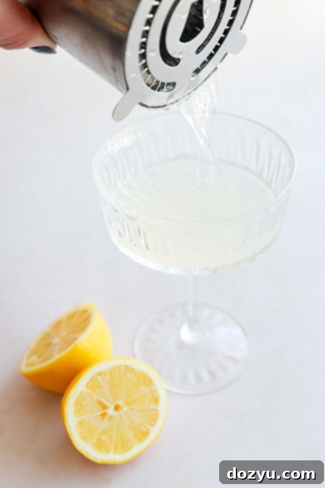 Sip on Perfection: The Bee's Knees Cocktail 4 pouring bees knees cocktail into a coupe glass with lemon halves