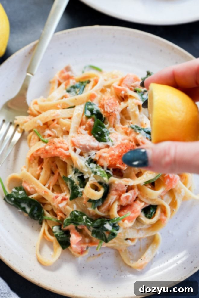 Velvety Lemon Salmon Pasta 6 hand squeezing lemon over a plate of creamy fettuccine with seafood and spinach