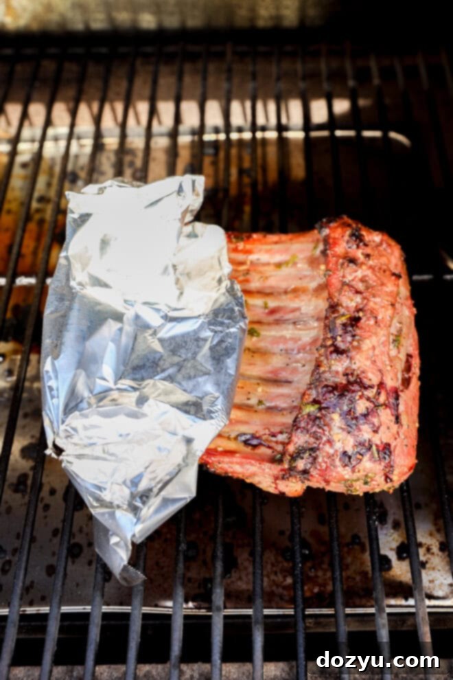 BBQ rack of lamb cooking on a grill with foil-wrapped bones for protection