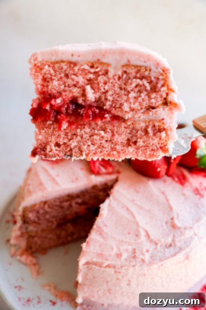 lifting a slice of strawberry cake with strawberry filling off of a cake plate