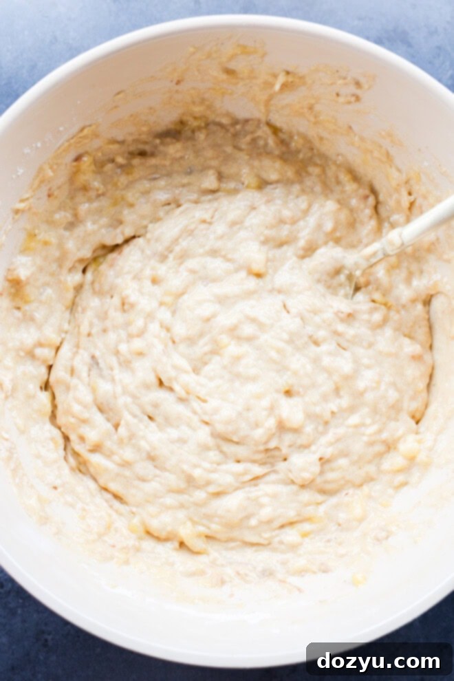 A spatula gently mixing banana chocolate chunk muffin batter in a large bowl, showcasing the rich texture.