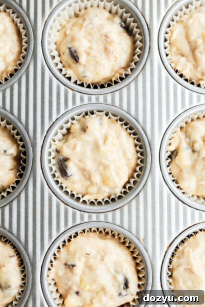 Unbaked banana chocolate chunk muffin batter generously topped with chocolate chips in a muffin tin, ready for the oven.