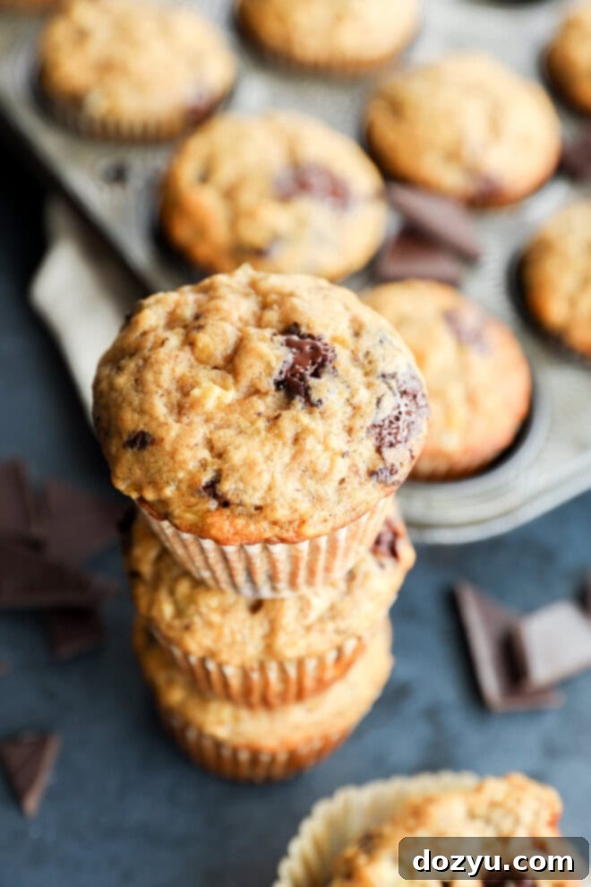 A stack of golden brown banana chocolate chunk muffins, perfectly baked, with visible melted chocolate.
