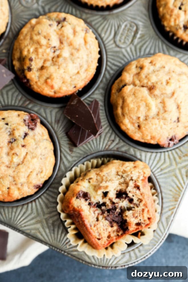 A banana chocolate chunk muffin with a bite taken out, revealing the soft interior and melted chocolate, sitting in a muffin tin.