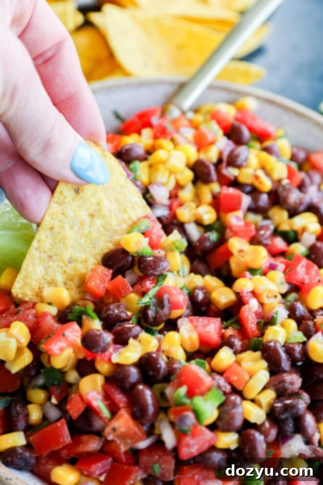 Southwestern Black Bean Corn Salsa Dip 6 hand dipping a chip into a combination of fresh veggies in a bowl
