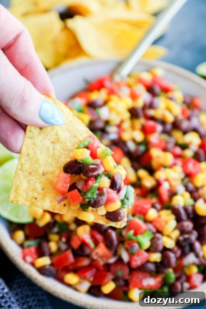 Southwestern Black Bean Corn Salsa Dip 7 hand holding tortilla chip with appetizer of veggies