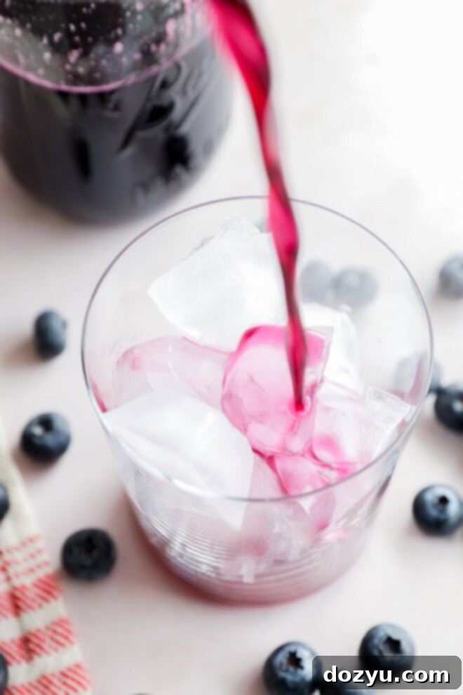 pouring blueberry simple syrup into a glass over ice