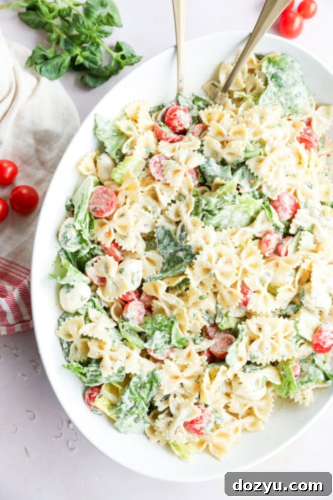 Sun-Kissed Caprese Bow Tie Salad 2 Easy mixture of vegetables and penne with creamy basil dressing in a large serving bowl, garnished with fresh basil leaves.