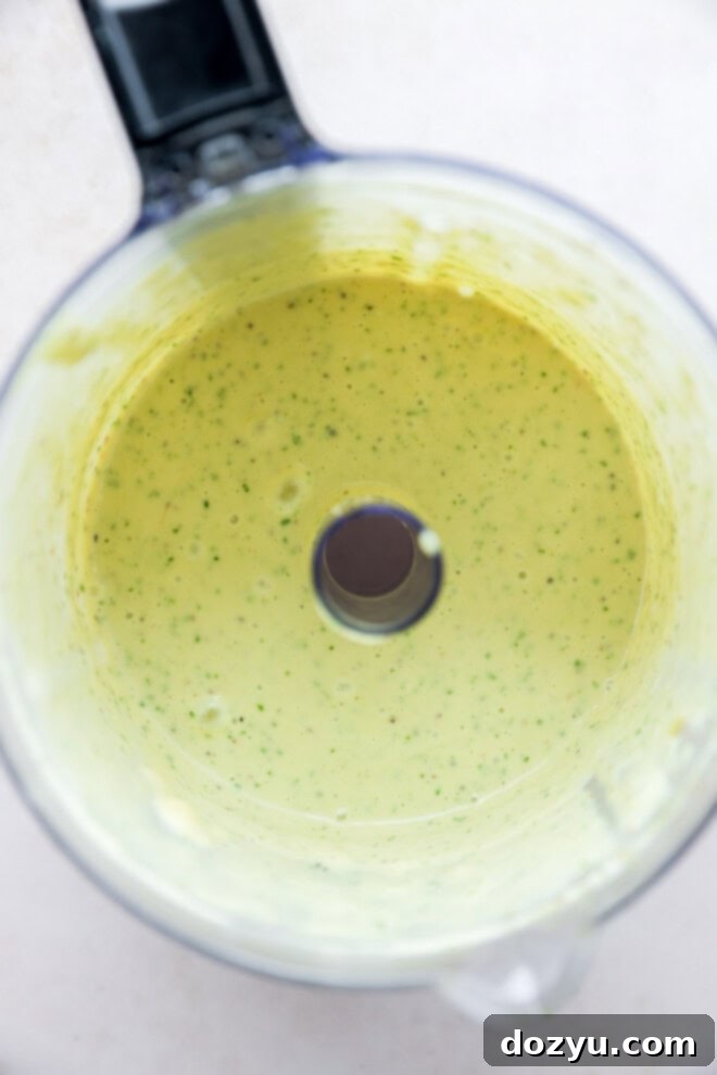 Sun-Kissed Caprese Bow Tie Salad 4 Basil dressing being blended in a food processor, showing its creamy texture and vibrant green color.