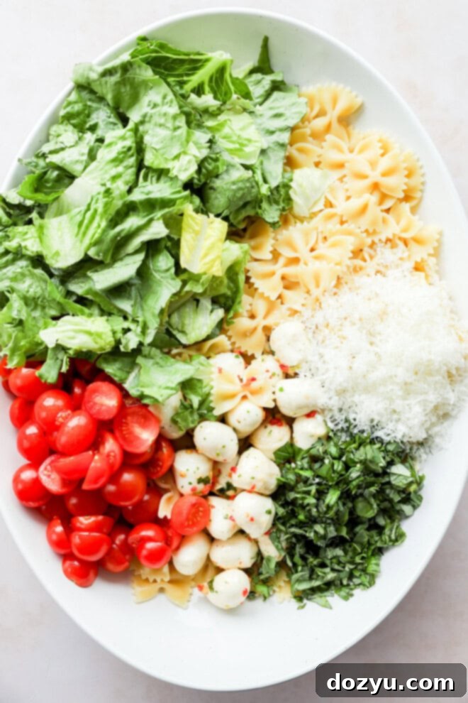 Sun-Kissed Caprese Bow Tie Salad 5 Ingredients for Caprese bow tie pasta salad, including cooked farfalle, chopped romaine, cherry tomatoes, mozzarella, and torn basil, placed in a large bowl before being mixed.