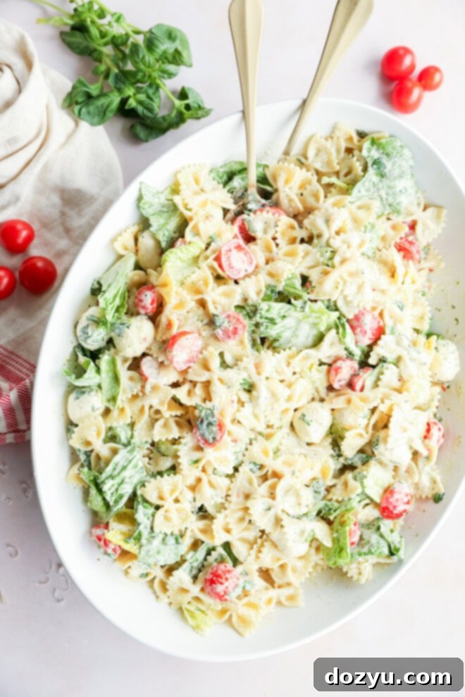 Sun-Kissed Caprese Bow Tie Salad 6 Caprese bow tie pasta salad served in a large bowl with two serving spoons, ready to be enjoyed.