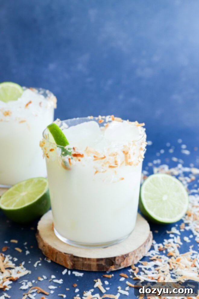 Easy tropical coconut margarita cocktail in glass on a coaster with fresh limes and coconut flakes for garnish
