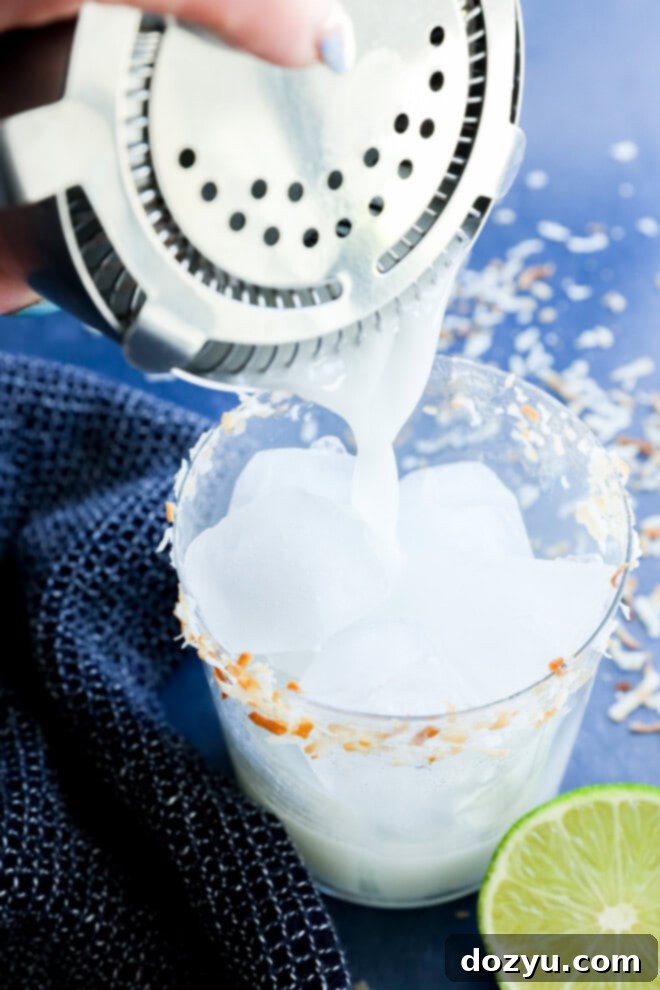 Pouring a creamy Coconut margarita into a cocktail glass with a toasted coconut rim