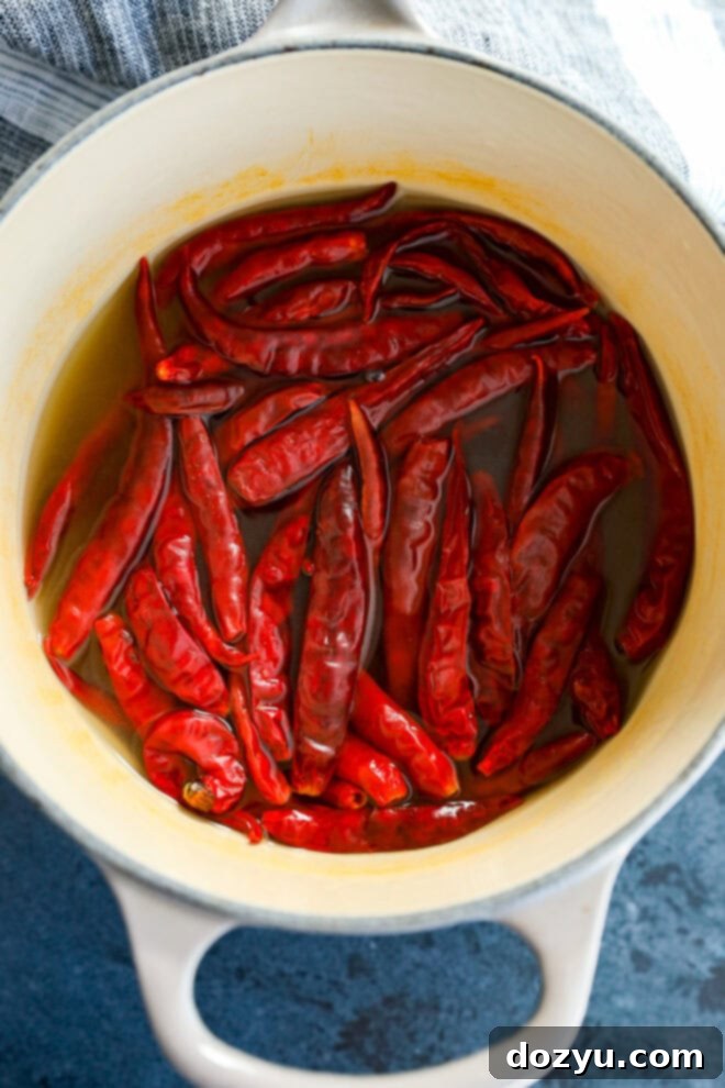 Dried chile de árbol peppers and a bouillon cube simmering in a small saucepan with water.