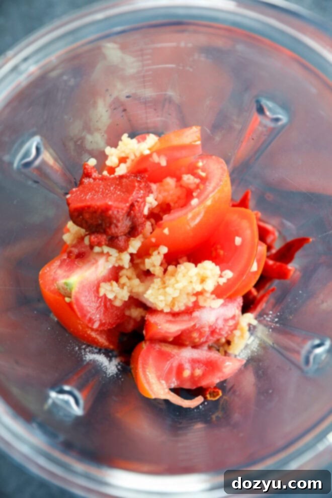 Plum tomatoes, tomato paste, and garlic cloves placed in a blender, ready for processing into salsa.