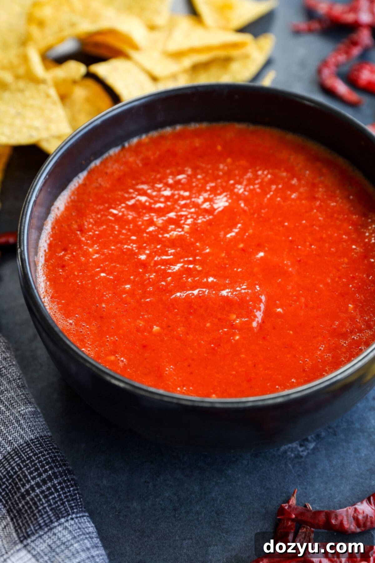 A bowl of vibrant red chile de árbol salsa surrounded by crispy tortilla chips.