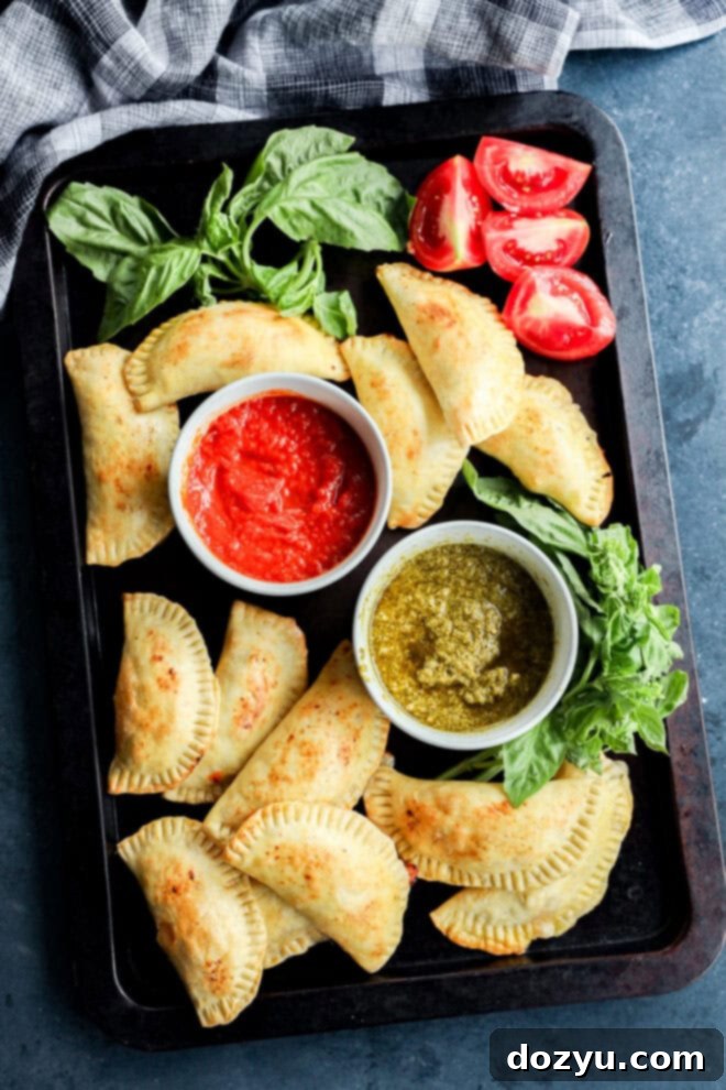 caprese empanadas on sheet pan with dipping sauces, fresh basil, and tomatoes