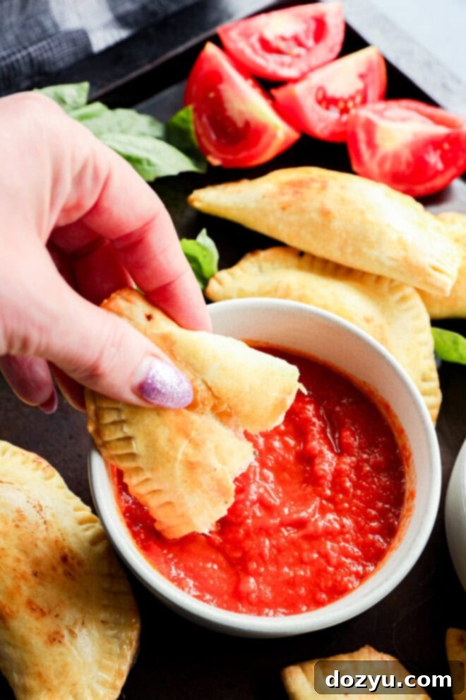 dipping a caprese empanada into a bowl of marinara sauce