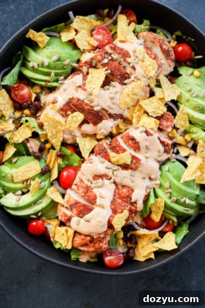 large bowl with healthy meal with lettuce, avocado, poultry, dressing, chips, seeds