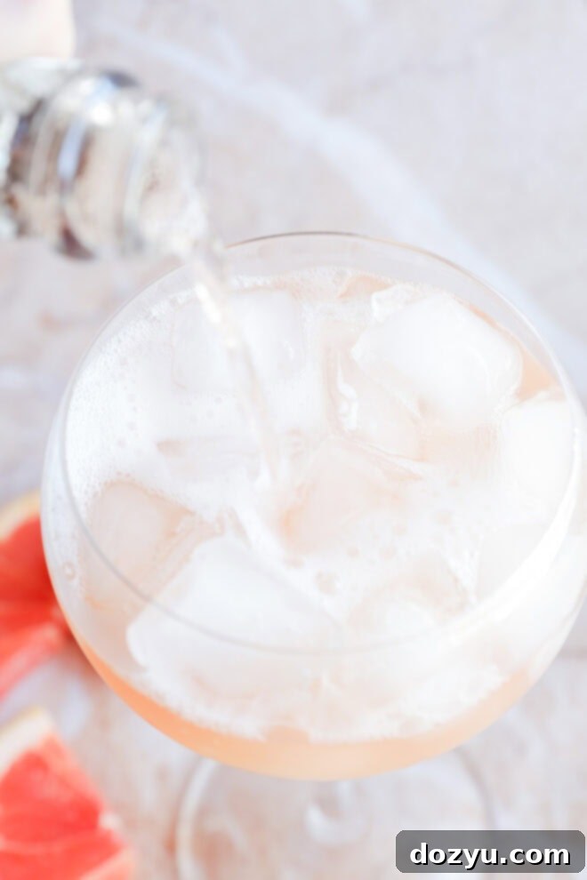 Pouring sparkling rośe into an elderflower cocktail on ice in a wine glass