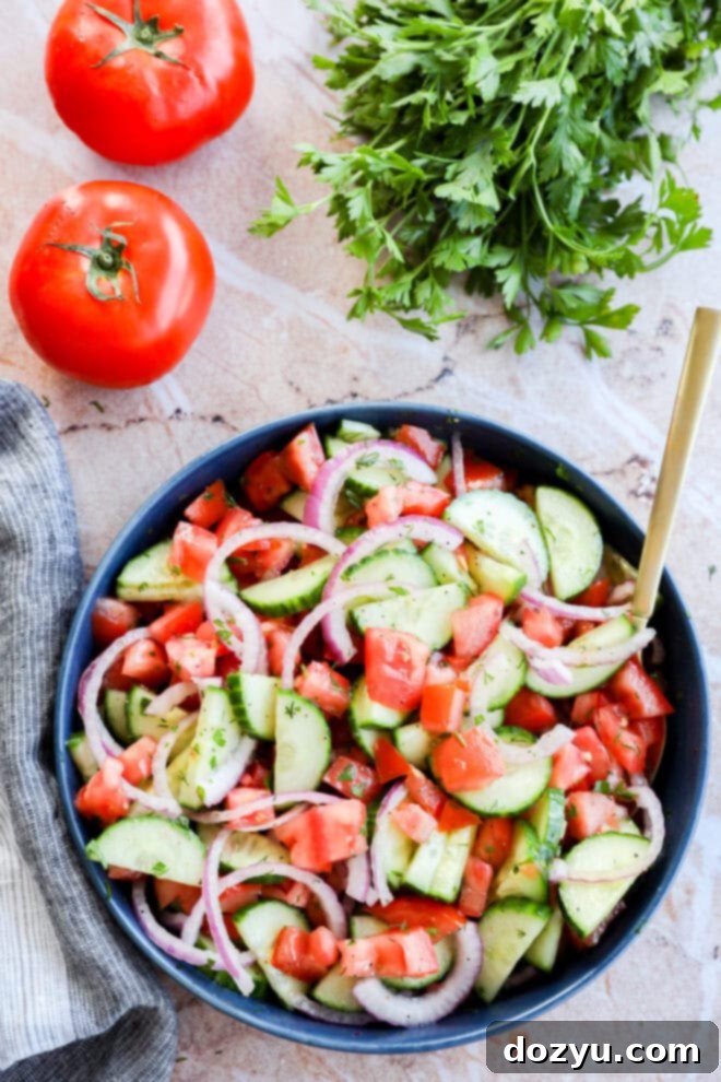 Summer Cucumber Tomato Salad 6 Image of Cucumber tomato salad in a bowl with gold spoon, fresh tomatoes and parsley in the background, ready to be served.
