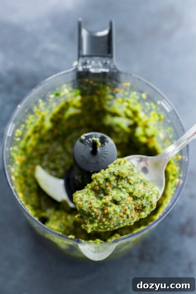 Vibrant Pistachio Pesto 7 A spoon gently lifts out a serving of vibrant pistachio pesto from the food processor after it has been freshly made, showcasing its creamy texture.