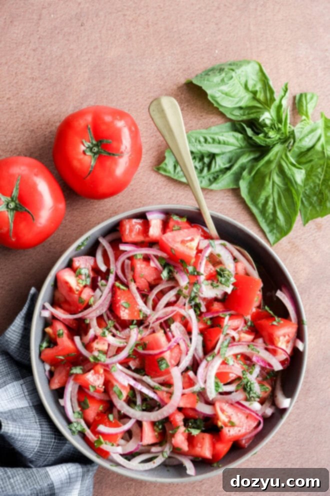 Tomato onion salad in large bowl with fresh tomatoes and fresh basil leaves