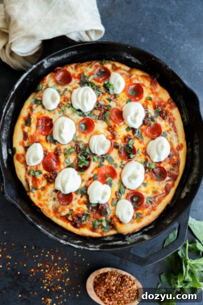 A freshly baked spicy pizza in a cast-iron skillet, topped with melted mozzarella cheese, pepperoni, and fresh basil, with a bowl of red pepper flakes and basil leaves nearby.