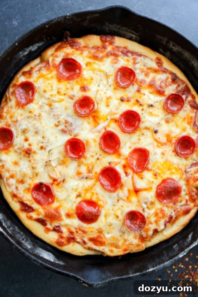 A freshly baked spicy pizza in a black cast iron skillet, topped with melted cheese and evenly spaced pepperoni slices.