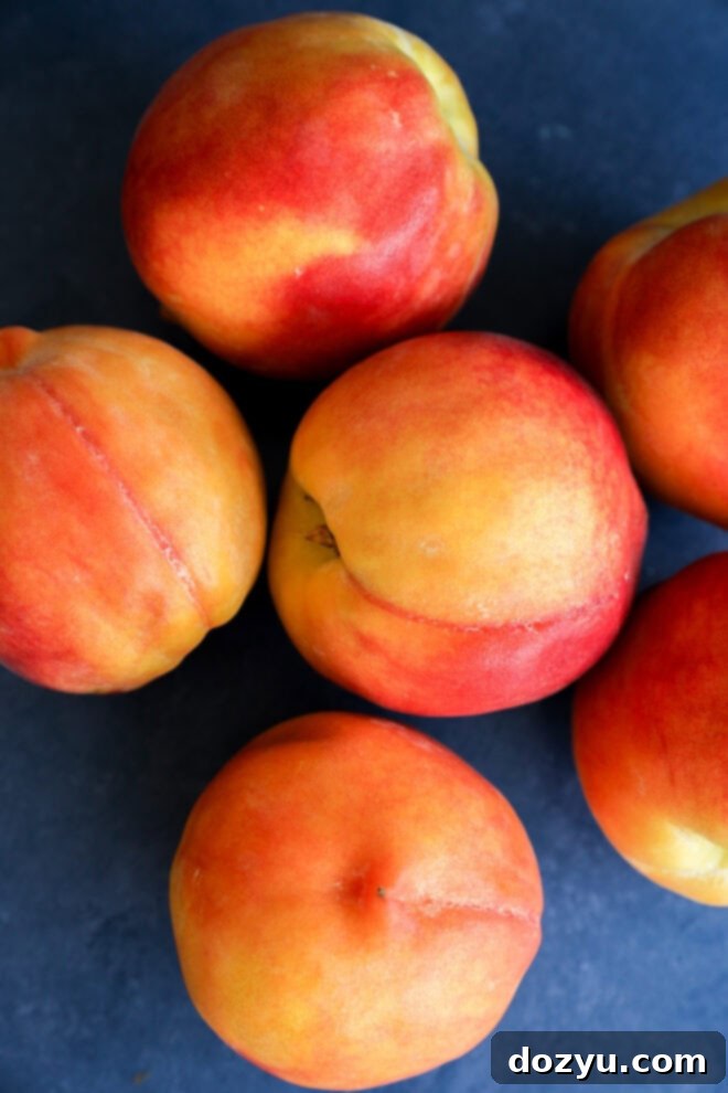 Six ripe nectarines with smooth, yellow-orange and red skin are arranged on a dark blue surface, perfect for slicing.