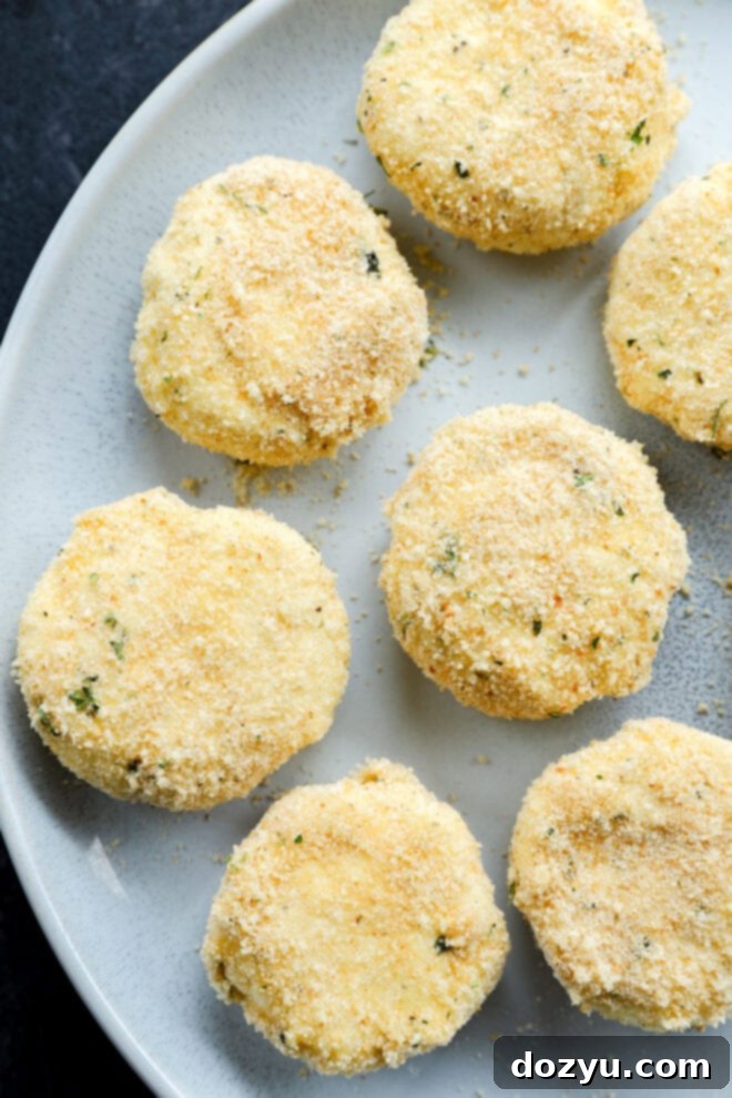 Seven breaded, round croquettes arranged on a light gray plate, viewed from above. The croquettes have a golden crust with small green herb flecks and a slightly rough, crumbly texture.