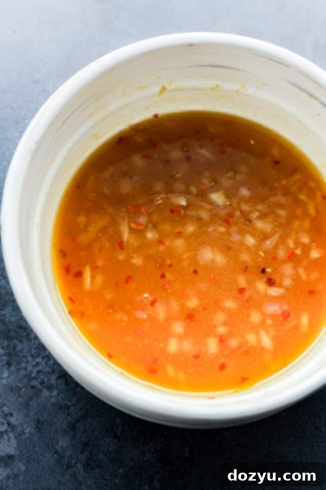 A white bowl filled with a reddish-orange sauce containing visible bits of minced garlic and red chili, set on a dark surface.