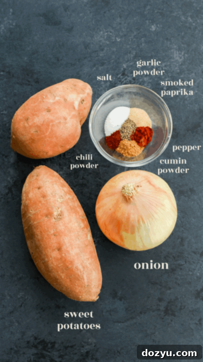 A beautifully arranged flat lay showing the essential ingredients for sweet potato breakfast potatoes on a dark surface. Featured prominently are two whole, unpeeled sweet potatoes, a perfectly peeled yellow onion, and a small, clear bowl containing a vibrant blend of ground spices including salt, garlic powder, smoked paprika, chili powder, cumin powder, and black pepper, all labeled for easy identification.
