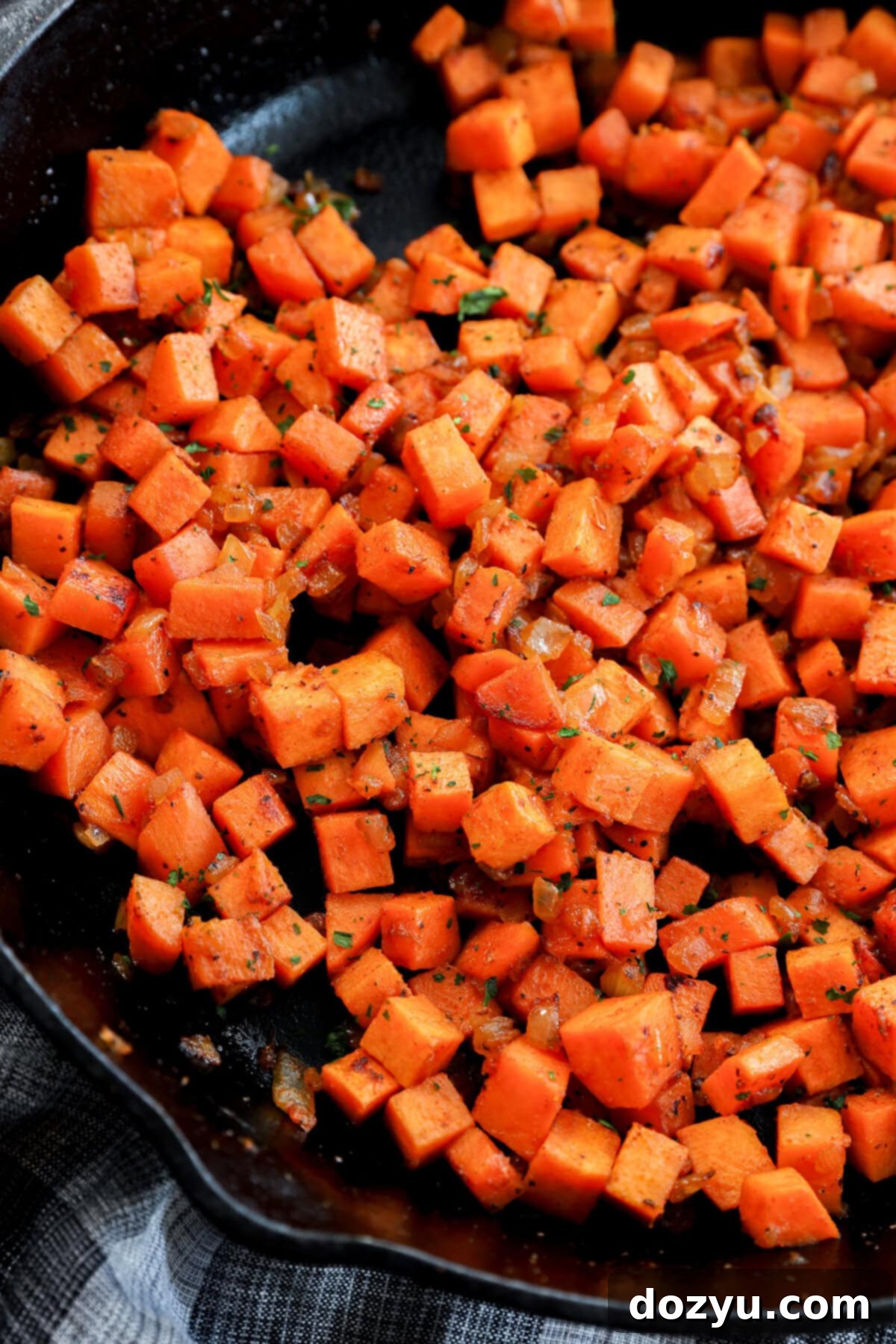 A beautiful close-up of crispy, perfectly sautéed sweet potato cubes seasoned with spices, served in a black skillet. The vibrant orange potatoes show golden-brown edges and a tender texture, ready to be enjoyed as a hearty breakfast or brunch side.