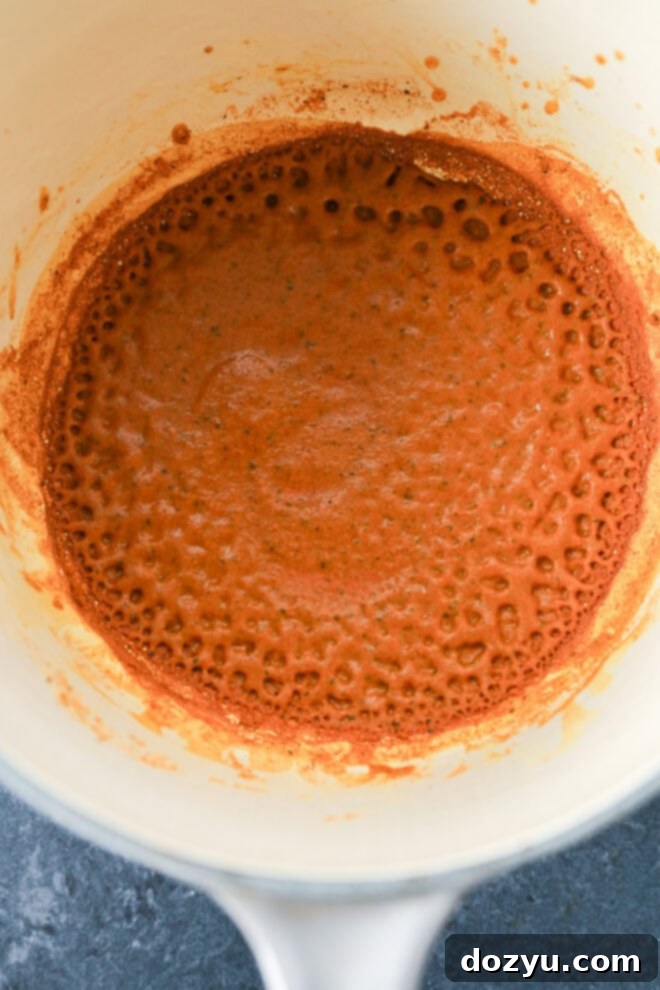 Golden Curried Chicken Salad 4 A close-up of a pot with bubbling tomato-based sauce, showing a reddish-brown color and frothy texture around the edges, set against a dark countertop.
