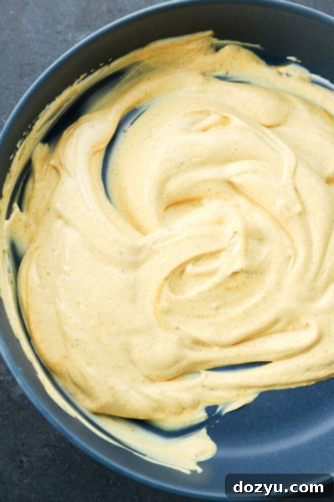 Golden Curried Chicken Salad 5 A close-up of a bowl containing creamy, yellow curry sauce with a smooth texture, swirled across the surface.