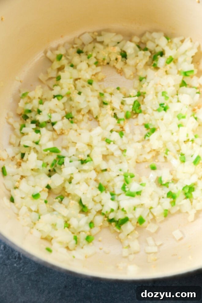 Diced onions, garlic, and green peppers are being sautéed in a light-colored pan, beginning the flavor base for a delicious creamy chicken tortilla soup.