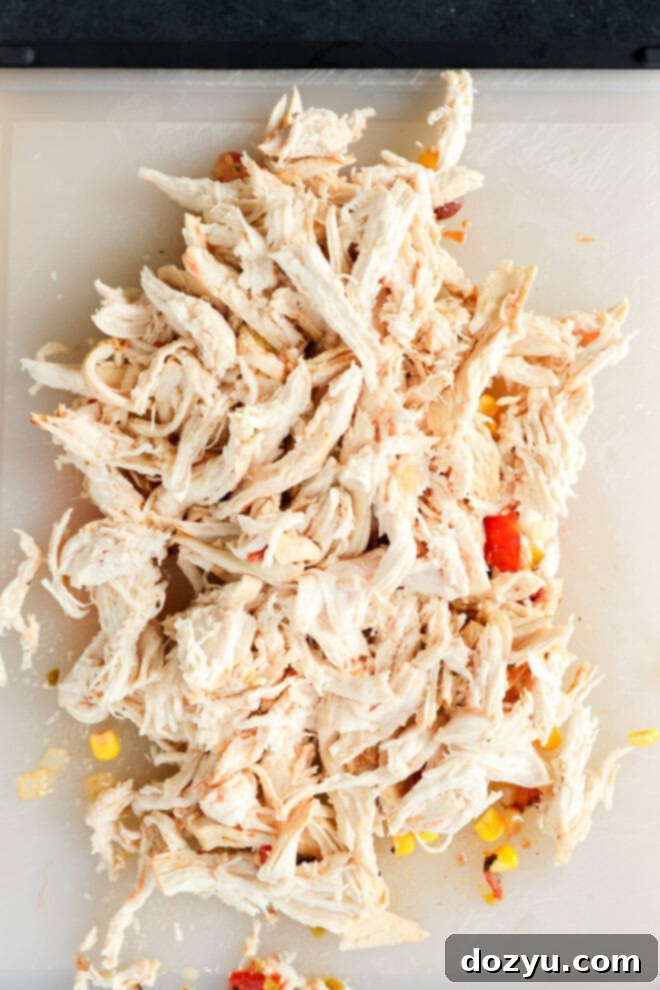 Shredded cooked chicken on a white cutting board, ready to be added back into the creamy chicken tortilla soup.