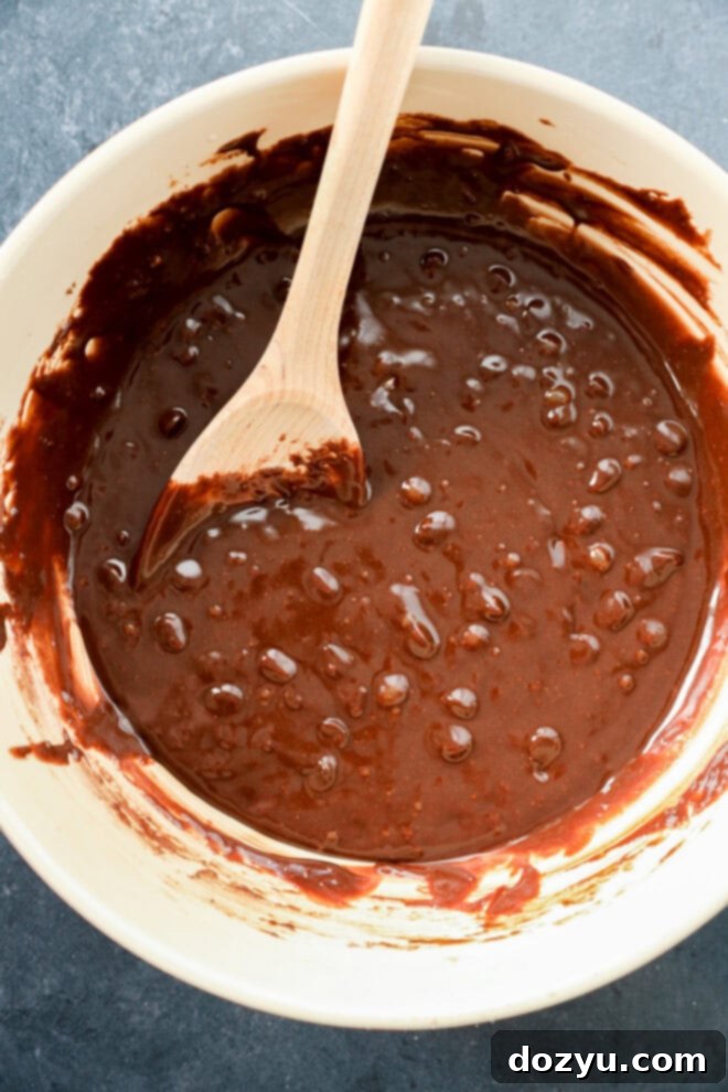 Spiced Pumpkin Fudge Brownies 4 A bowl of brownie batter with a wooden spoon resting inside. The batter is thick and glossy with some air bubbles visible on the surface. The bowl sits on a dark countertop.