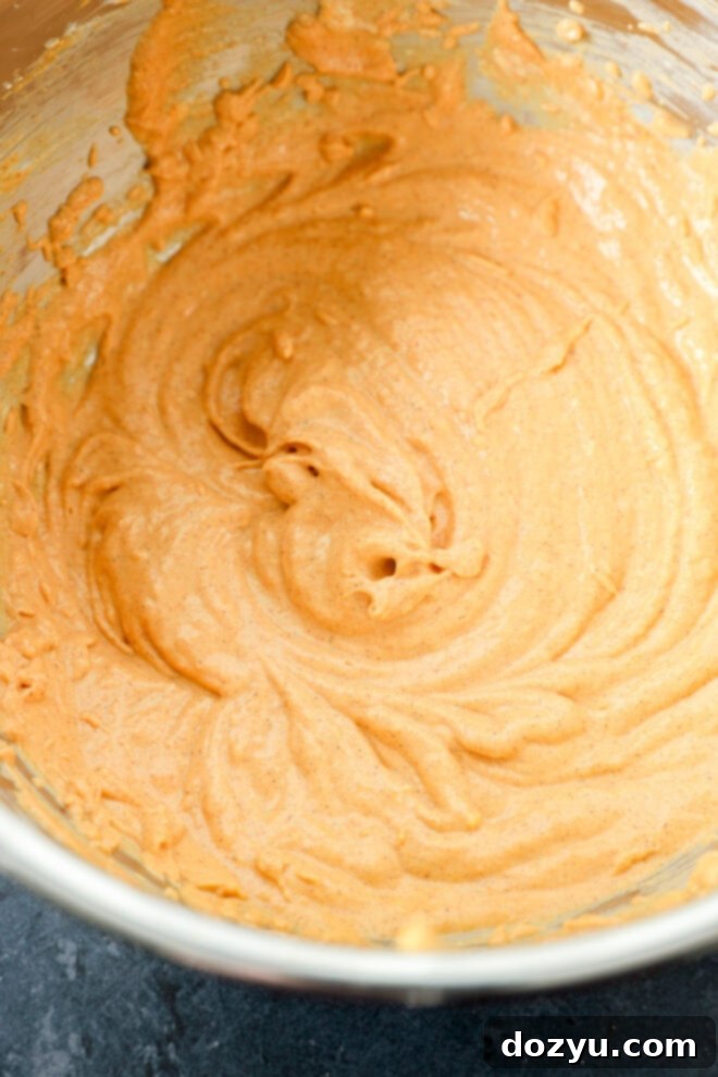 Spiced Pumpkin Fudge Brownies 5 A metal mixing bowl filled with creamy, light brown batter, swirled smoothly, sitting on a dark countertop.