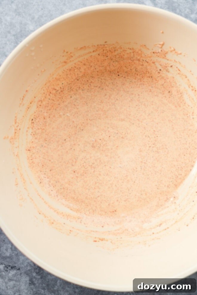 A beige mixing bowl containing a creamy, spiced dressing on a grey kitchen counter, ready for the salad ingredients.