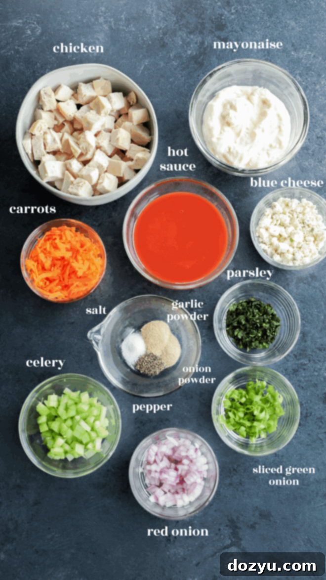 A top-down view of bowls containing diced chicken, mayonnaise, hot sauce, blue cheese, shredded carrots, chopped parsley, seasonings, and veggies—perfect inspiration for meal prep for buffalo chicken salad.