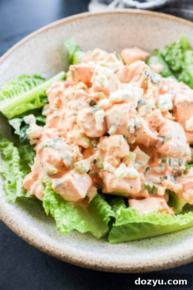 A bowl of salad with chunks of chicken mixed in a creamy orange dressing, placed on a bed of fresh green romaine lettuce leaves for buffalo chicken salad.