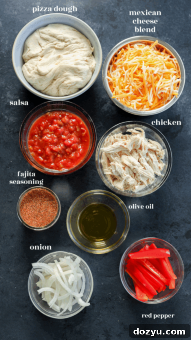 Sizzling Fajita Pizza 3 Overhead view of ingredients in bowls: pizza dough, shredded Mexican cheese blend, salsa, shredded chicken, fajita seasoning, olive oil, sliced onion, and sliced red pepper on a dark surface.