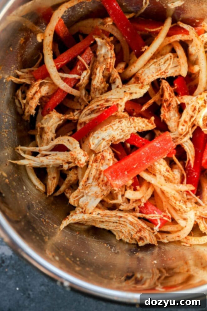 Sizzling Fajita Pizza 4 Shredded chicken mixed with sliced red bell peppers and onions, all seasoned with spices, in a metal bowl.