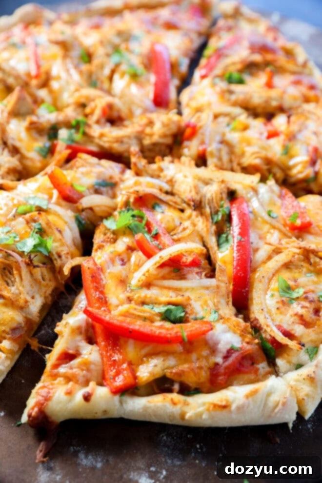 Sizzling Fajita Pizza 5 Close-up of a sliced pizza topped with melted cheese, shredded chicken, red bell pepper strips, onions, and fresh cilantro on a thick, crispy crust.