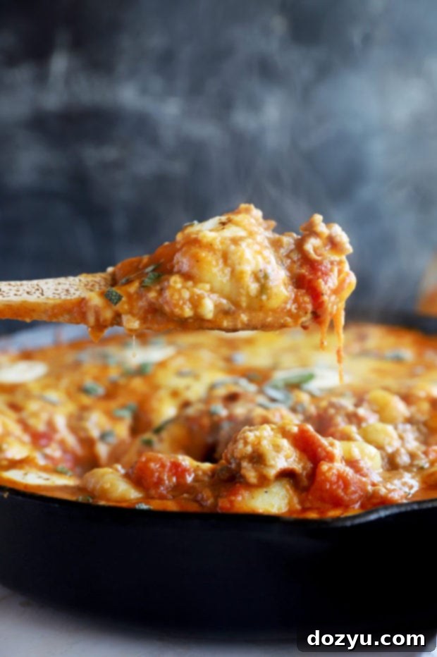 A fork holds a perfectly cooked piece of pumpkin gnocchi, lifted from a rustic bake, illustrating the tender texture and rich autumnal flavor of the dish.