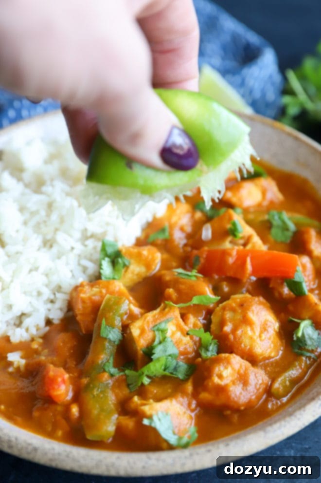 A hand gently squeezes fresh lime juice over a steaming bowl of rich pumpkin chicken curry and fluffy rice, adding a bright, zesty finish to the savory dish.